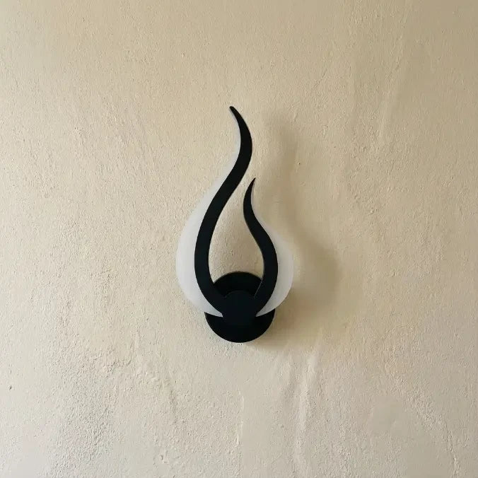 Veilleuse murale flamme éteinte au design courbe noir et blanc sur mur crème en lumière naturelle.