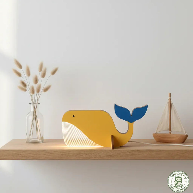 Veilleuse baleine en bois posée sur une étagère avec un petit bateau. Idéale pour une décoration de chambre bébé sur le thème marin.