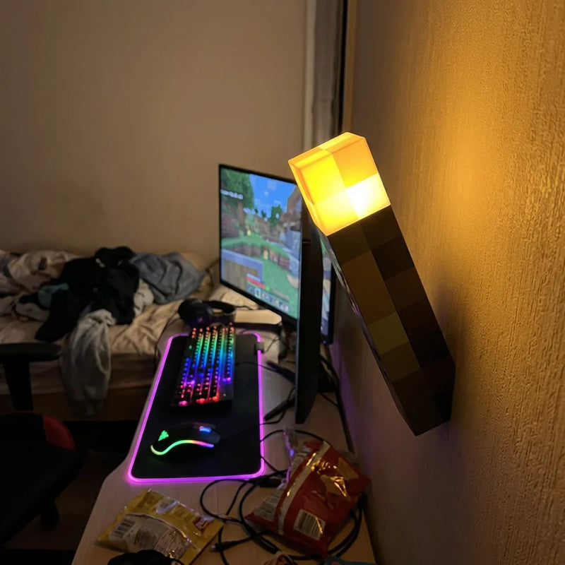 Photographie authentique d'une applique murale torche Minecraft fixée au mur d'une chambre, finalisant la décoration immersive d'un setup gamer.