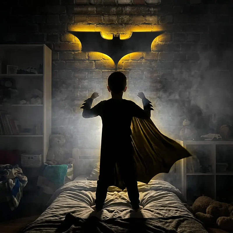 Silhouette garçon en cape face à une veilleuse murale Batman illuminant une chambre d'enfant style super-héros.