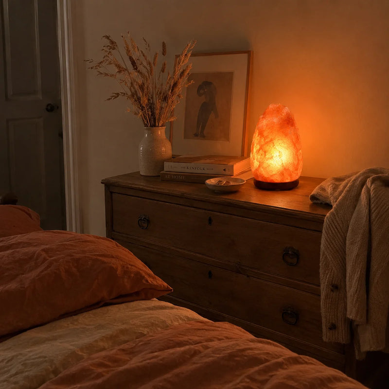 Lampe à sel allumée sur une commode dans une chambre aux tons terracotta le soir – Tendre Veilleuse