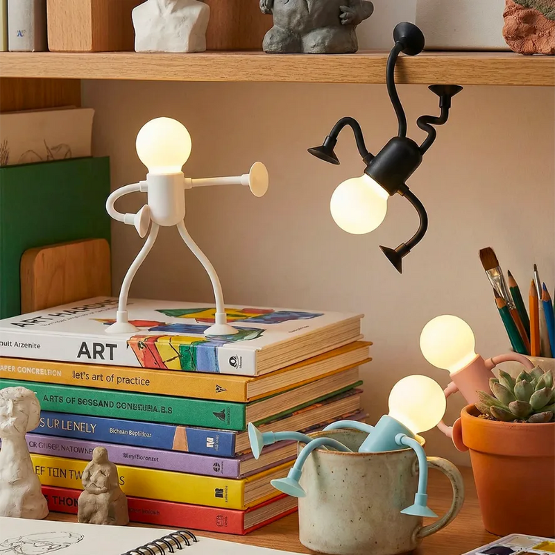 Mise en scène créative sur un bureau : une lampe robot noire est suspendue à l'envers sur l'étagère, tandis qu'une blanche éclaire des livres d'art et une bleue repose dans un pot à crayons. Ces lampes articulées au design original apportent une touche ludique à la décoration d'une chambre d'ado ou d'un studio d'étudiant.