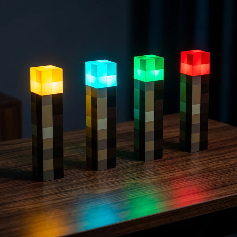 Lampe de bureau torche Minecraft alignée en 4 exemplaires affichant les couleurs LED RGB : jaune chaud, cyan, vert émeraude et rouge profond.