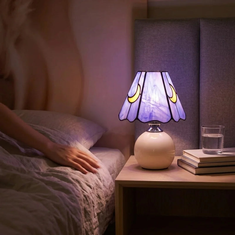 Lampe de chevet céramique vitrail violet allumée sur table de nuit en bois, ambiance chambre adulte avec lumière violette douce et draps en lin — Tendre Veilleuse