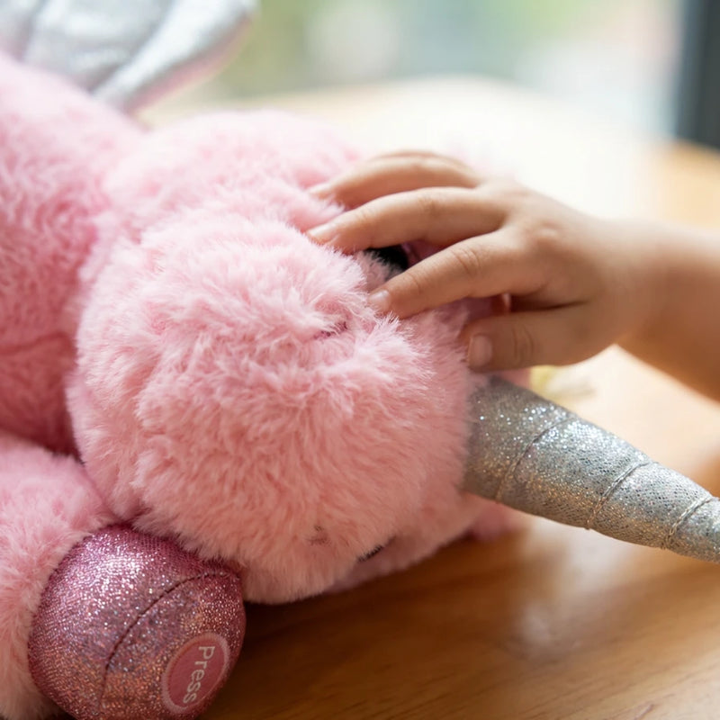 Gros plan sur le bouton d'allumage "Press" brodé sur la patte de la veilleuse licorne et main d'enfant caressant sa texture ultra-douce.