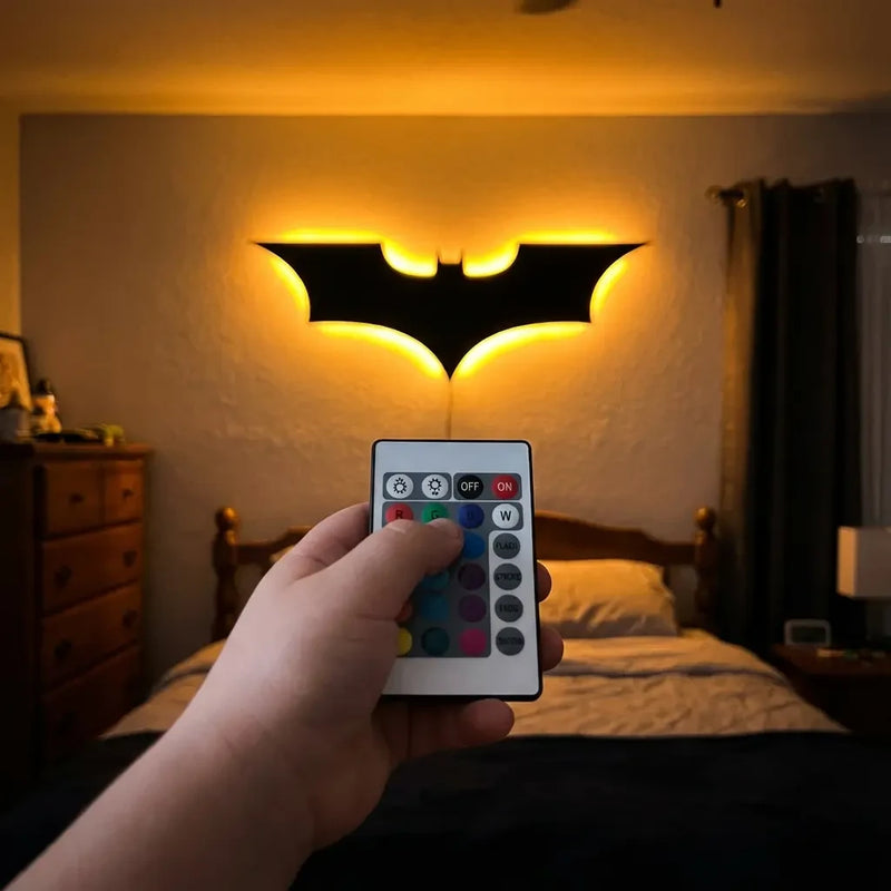 Main réglant une veilleuse murale Batman avec télécommande RGB dans une chambre à coucher.