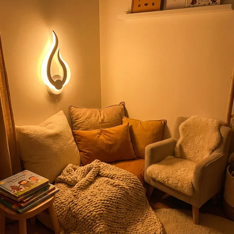 Coin lecture cosy avec fauteuil et plaids éclairé par une veilleuse murale flamme douce et apaisante.