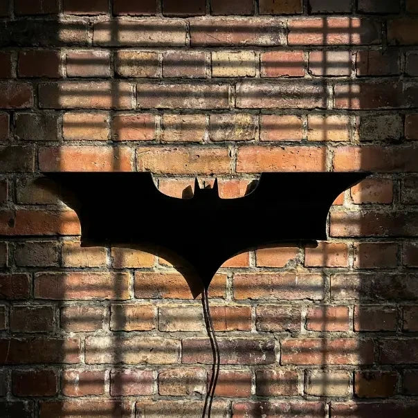 Veilleuse murale Batman noire éteinte sur mur de briques rouges en lumière naturelle.