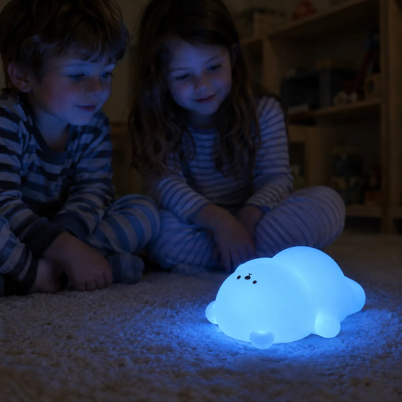 Veilleuse ours allumée en bleu sur un tapis devant deux enfants en pyjama le soir, Tendre Veilleuse