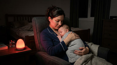 Maman allaitant son bébé la nuit, éclairée par une veilleuse à lumière rouge pour préserver la mélatonine du lait maternel et favoriser le rendormissement.