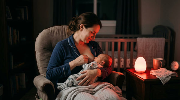 Maman allaitant son bébé la nuit éclairée par une veilleuse rouge en forme d'oeuf sur la table de chevet — Tendre Veilleuse