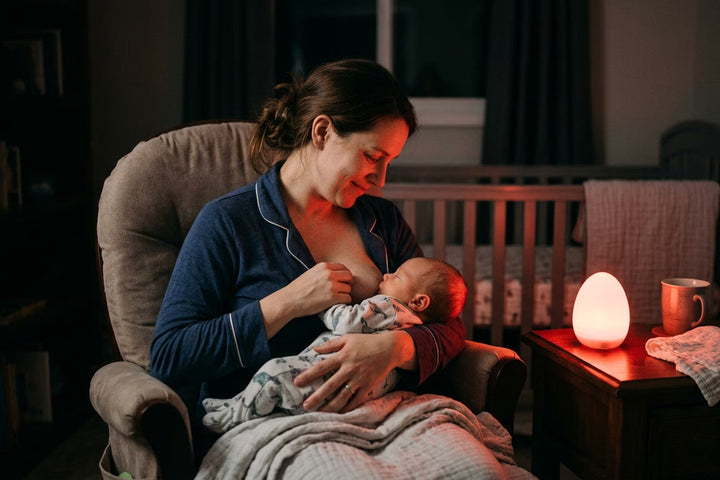 Maman allaitant son bébé la nuit éclairée par une veilleuse rouge en forme d'oeuf sur la table de chevet — Tendre Veilleuse