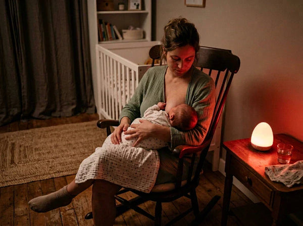 Mère allaitant son nouveau-né la nuit éclairée uniquement par une veilleuse à lumière rouge