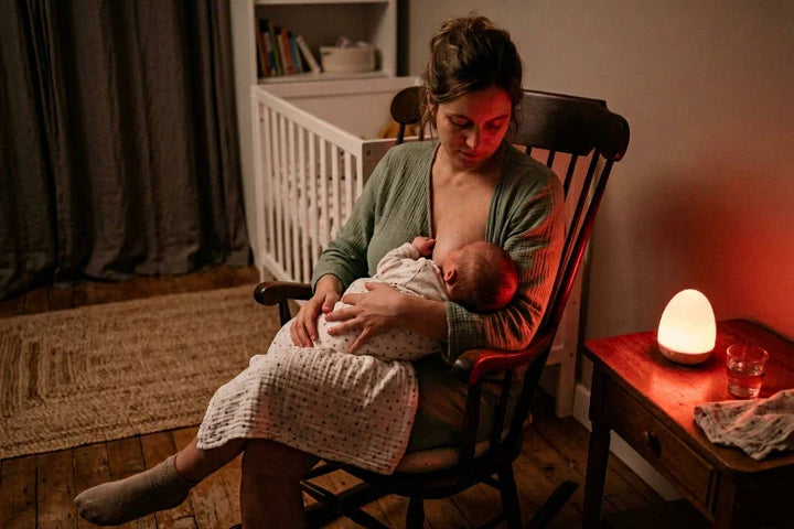 Mère allaitant son nouveau-né la nuit éclairée uniquement par une veilleuse à lumière rouge