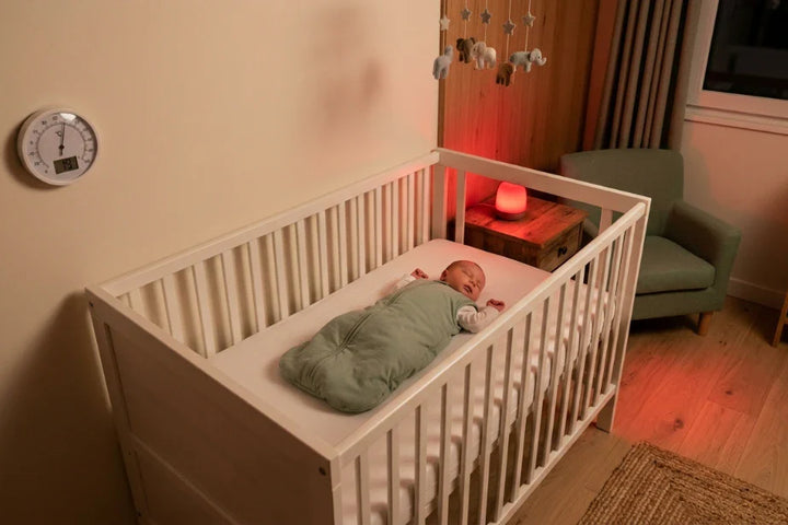 Chambre de bébé la nuit avec thermomètre indiquant 19°C, veilleuse rouge douce et bébé endormi en gigoteuse verte — Tendre Veilleuse