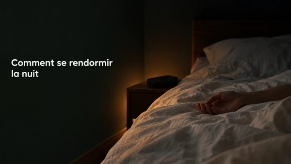 Chambre la nuit, une main posée sur la couette et le réveil retourné face contre la table de chevet, éclairée par une lumière ambrée basse