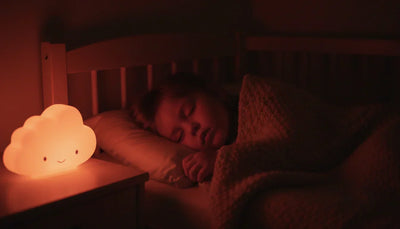 Enfant de 3 ans dormant paisiblement dans son lit, éclairé par une veilleuse nuage diffusant une lumière rouge douce idéale pour la production de mélatonine.