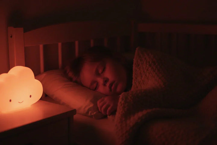 Enfant de 3 ans dormant paisiblement dans son lit, éclairé par une veilleuse nuage diffusant une lumière rouge douce idéale pour la production de mélatonine.