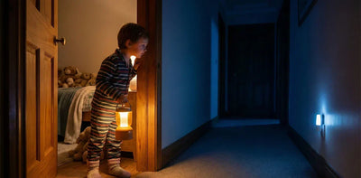 Enfant de 5 ans traversant un couloir sombre avec une veilleuse nomade pour aller aux toilettes seul. Solution naturelle contre l'énurésie secondaire (pipi au lit) causée par la peur du noir et le stress nocturne.