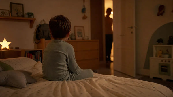 Enfant de quatre ans assis dans son lit, porte entrouverte et parent dans le couloir éclairé, Tendre Veilleuse