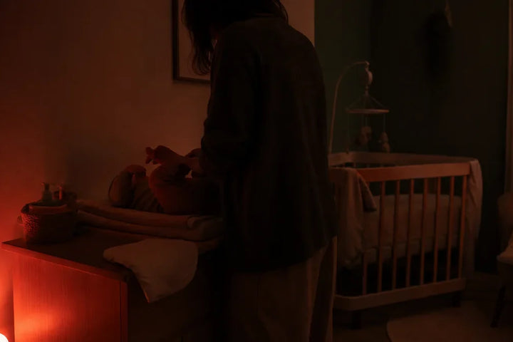 Chambre de bébé éclairée par une lumière rouge de très faible intensité pendant un change nocturne, Tendre Veilleuse