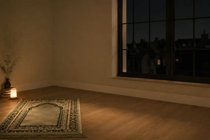 Tapis de prière déroulé devant une fenêtre en pleine nuit, éclairé par une lumière chaude et basse