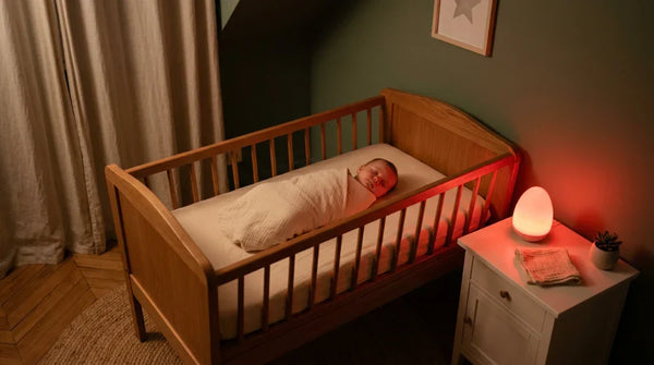 Rituel du coucher bébé sous lumière rouge 631 nm dans une chambre apaisée, nourrisson somnolent dans son lit en bois, veilleuse rouge allumée — Tendre Veilleuse