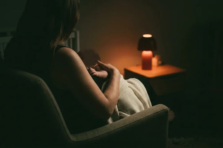 Bébé allaité endormi contre sa mère pendant une tétée de nuit éclairée en lumière rouge tamisée