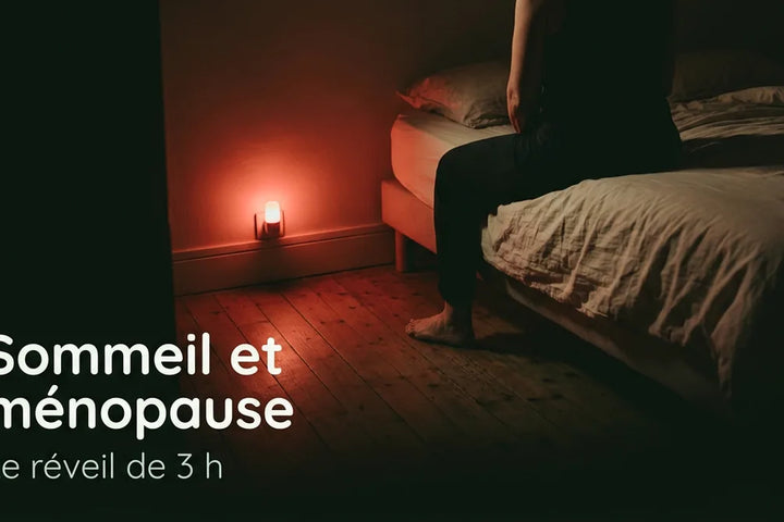 Femme d'une cinquantaine d'années assise au bord de son lit la nuit, éclairée uniquement par une veilleuse rouge placée au sol