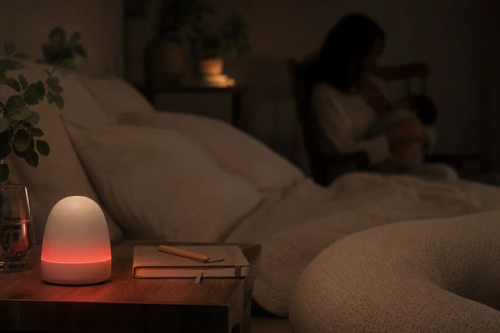 Veilleuse allaitement lumière rouge posée sur table de nuit pendant tétée nocturne, ambiance sombre apaisante, Tendre Veilleuse