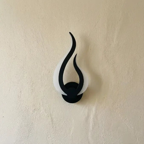 Veilleuse murale flamme éteinte au design courbe noir et blanc sur mur crème en lumière naturelle.