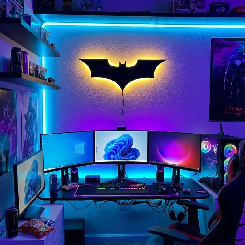 Setup gaming PC avec écrans multiples et veilleuse murale Batman sous éclairage néon bleu et violet.