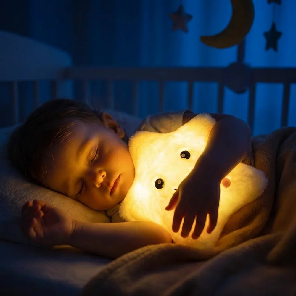 Bébé qui dort paisiblement dans son lit en serrant contre lui un doudou lumineux étoile diffusant une lumière jaune tamisée rassurante.