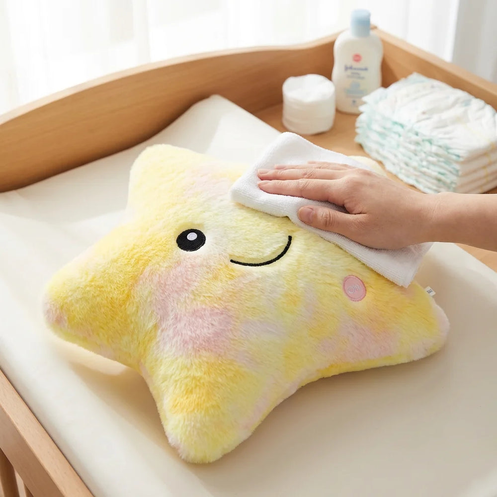 Main nettoyant délicatement la surface de la peluche lumineuse étoile avec un chiffon doux sur une table à langer, montrant son entretien hygiénique.