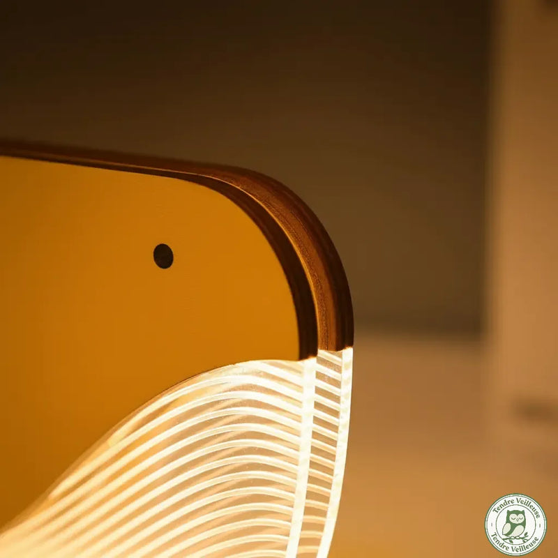 Gros plan sur la lampe baleine en bois massif et ses stries en acrylique diffusant une lumière LED blanc chaud non éblouissante.