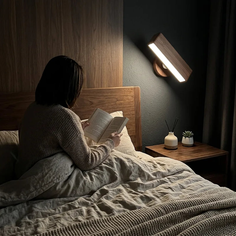 Applique murale bois pivotée éclairant une personne qui lit dans un lit en lin froissé, table de chevet en noyer, ambiance cocon fin de journée — Tendre Veilleuse