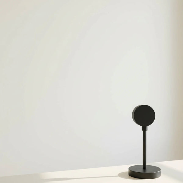 Lampe projecteur coucher de soleil noire éteinte sur un support, posée sur une surface blanche avec un fond blanc épuré.