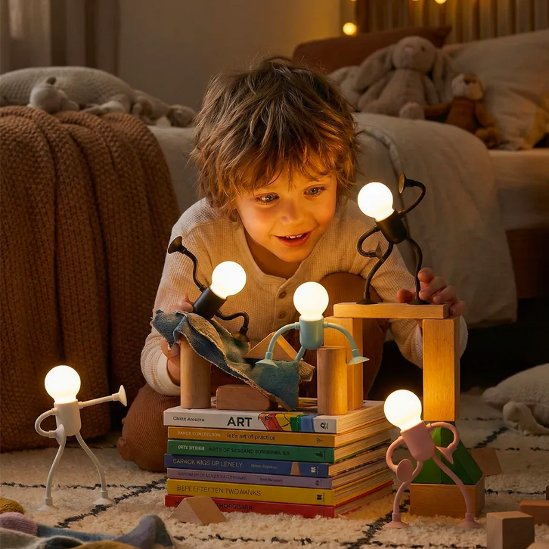 Petit garçon jouant joyeusement au sol dans sa chambre avec une collection de lampes robots articulées lumineuses. Ces veilleuses sans fil servent à la fois d'éclairage d'ambiance rassurant et de jouet créatif, stimulant l'imagination des enfants.