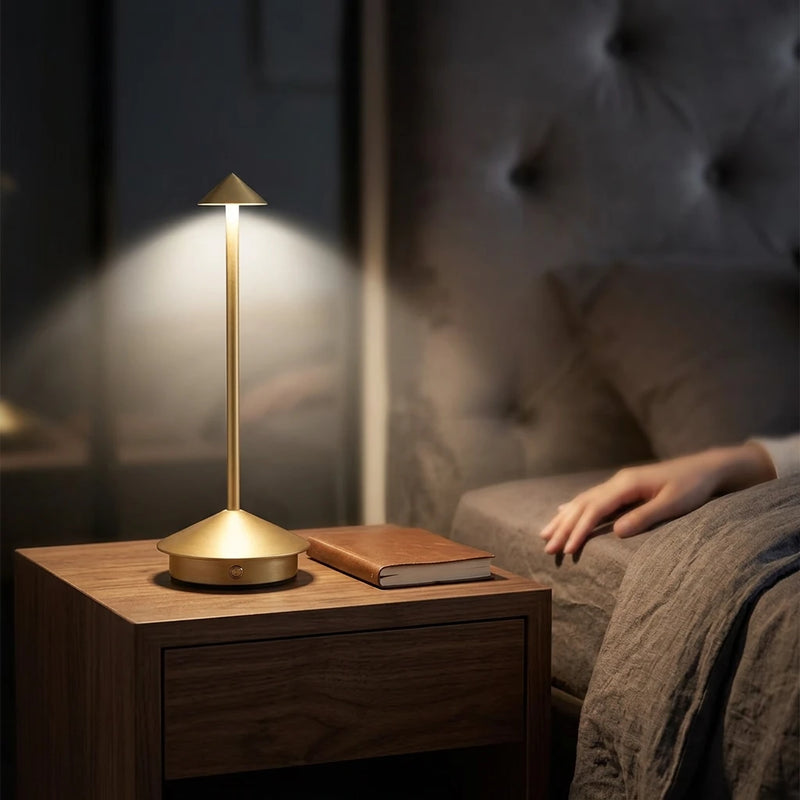Lampe de chevet tactile aluminium allumée en lumière neutre sur
table de nuit bois sombre, ambiance lecture coucher avec draps
lin, main posée au premier plan — Tendre Veilleuse