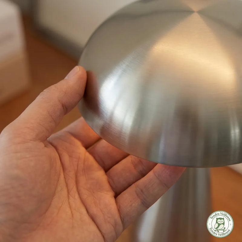 Gros plan main posée sur le chapeau champignon en métal
brossé, démonstration de la commande tactile — Tendre Veilleuse