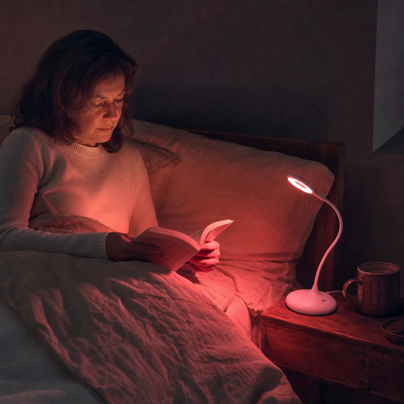 Femme lisant au lit à la lumière rouge de la lampe posée sur la table de chevet, chambre dans l'obscurité