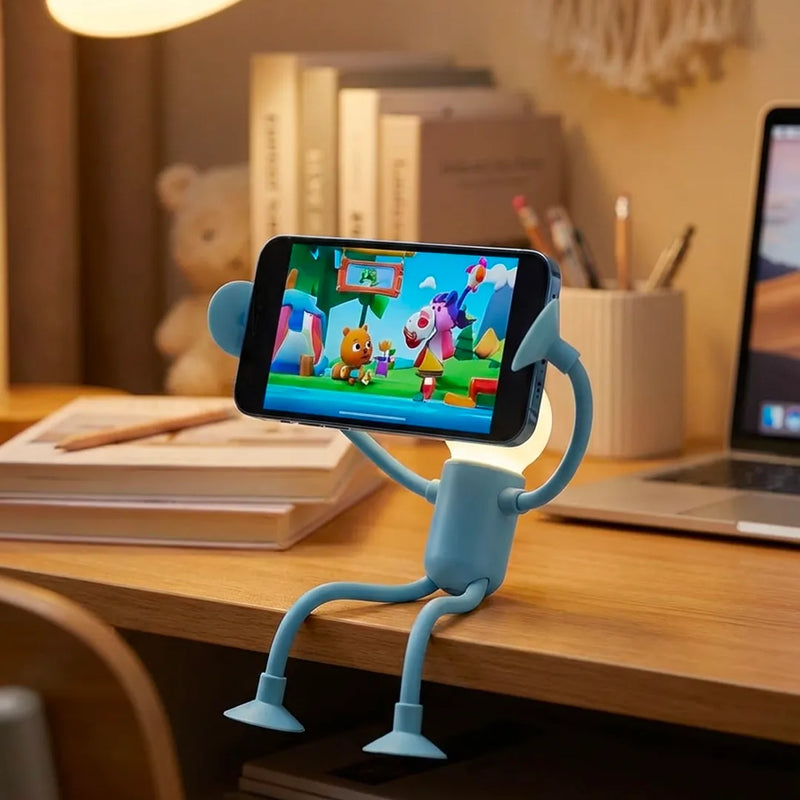 Lampe robot bleue assise au bord d'un bureau, utilisée comme support de téléphone stable pour regarder une vidéo. Ce gadget de bureau ludique permet de poser son smartphone en mode main-libre, idéal pour les ados ou le télétravail.