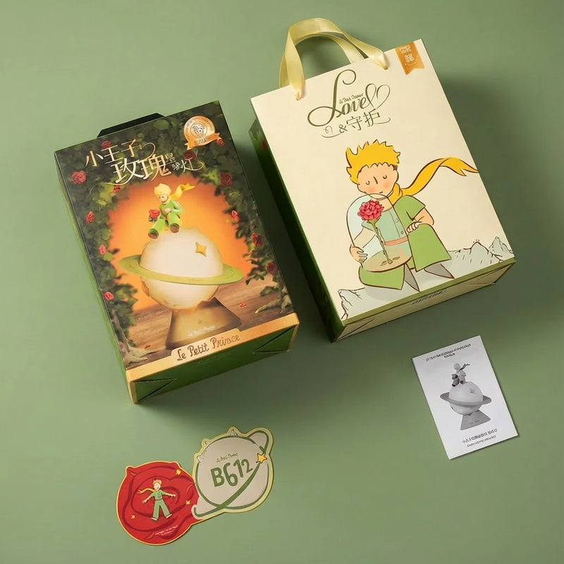 Vue d'ensemble du packaging de la Veilleuse Petit Prince : boîte illustrée verte, sac cadeau beige avec le Prince, stickers B612 et notice, un ensemble parfait pour un cadeau de naissance.