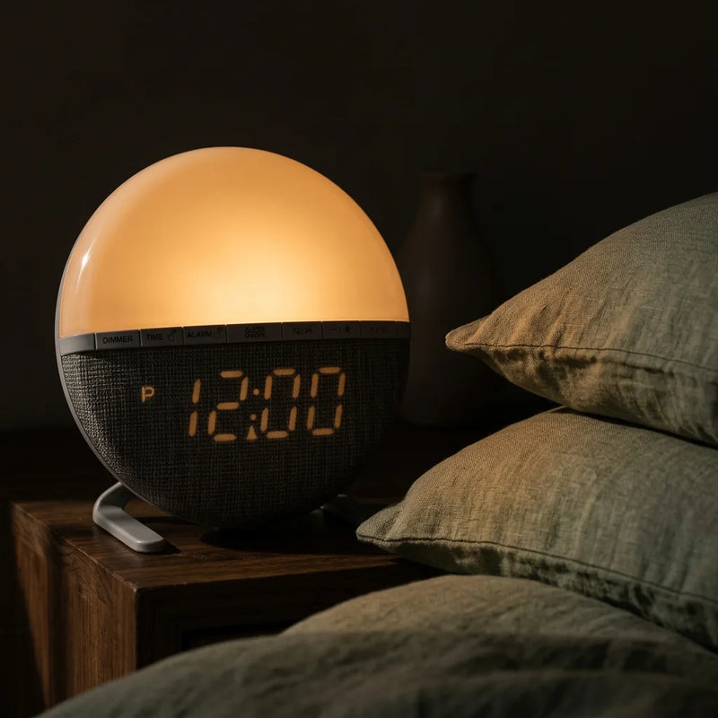 Réveil simulateur d'aube compact posé sur table de chevet en bois, lumière chaude diffuse, affichage 12h00