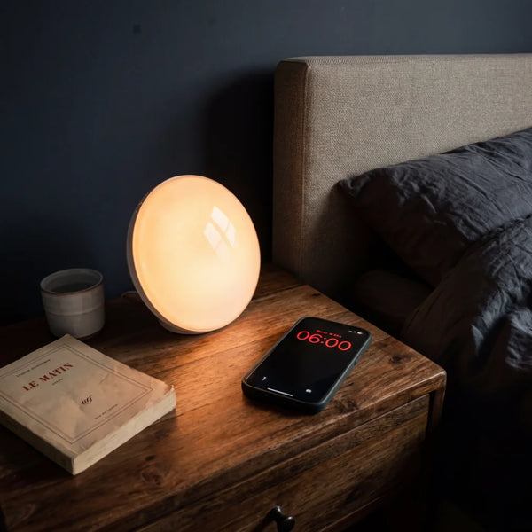 Simulateur d'aube lumière ambrée comparé à un réveil téléphone 6h du matin sur table de nuit