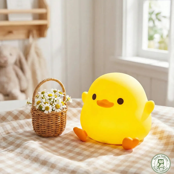 Veilleuse canard silicone jaune Quacko éteinte posée sur nappe vichy à côté d'un panier de marguerites, décor chambre enfant — Tendre Veilleuse