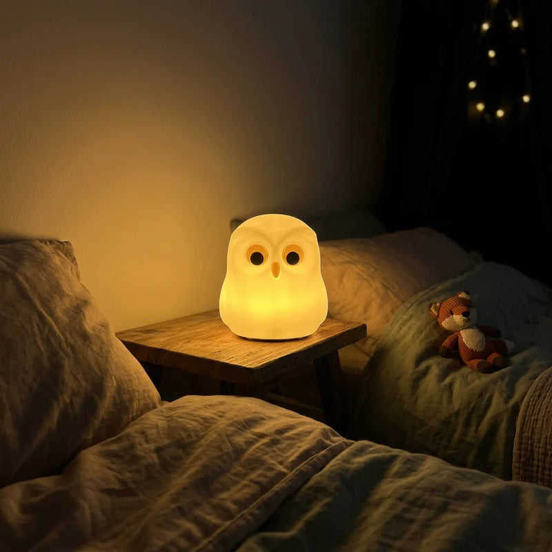 Veilleuse hibou silicone allumée en mode lumière chaude dorée, posée sur table de chevet en bois dans chambre obscure, ambiance cosy rassurante, Tendre Veilleuse