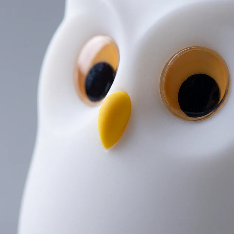 Gros plan sur les yeux mobiles expressifs et le bec nez jaune en silicone de la veilleuse hibou, texture silicone souple blanc mat, Tendre Veilleuse