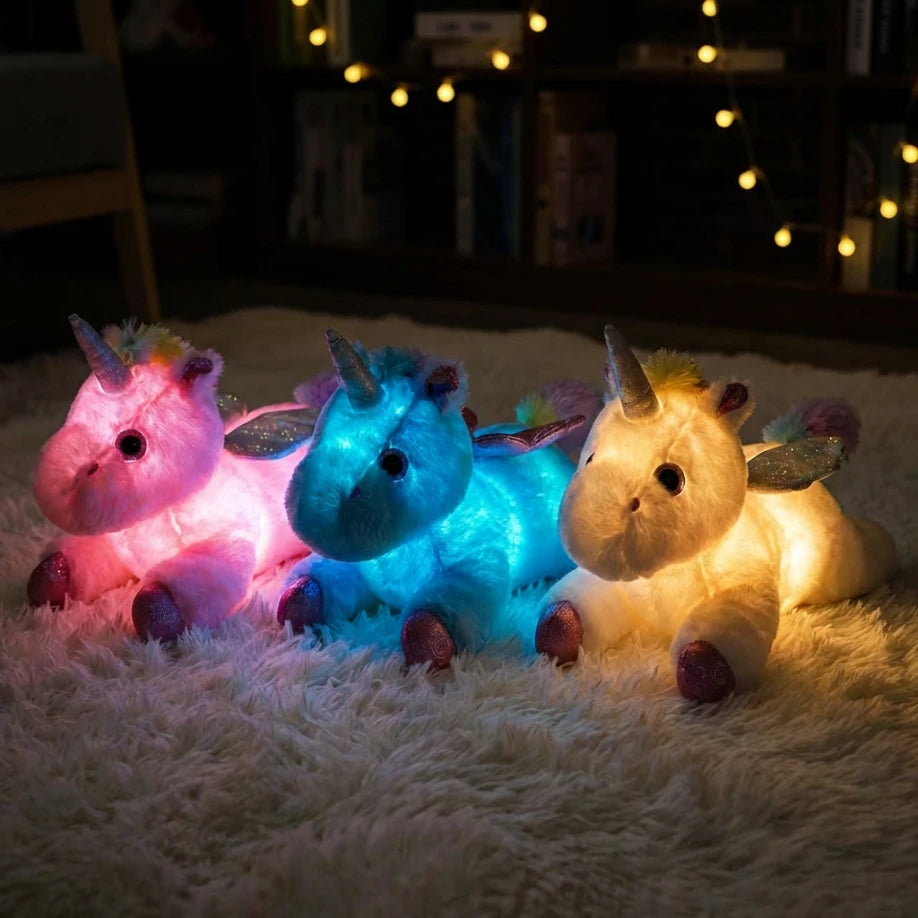 Trio de peluches veilleuses licornes illuminées en rose, bleu et jaune, illustrant les variations de couleurs LED apaisantes dans le noir.