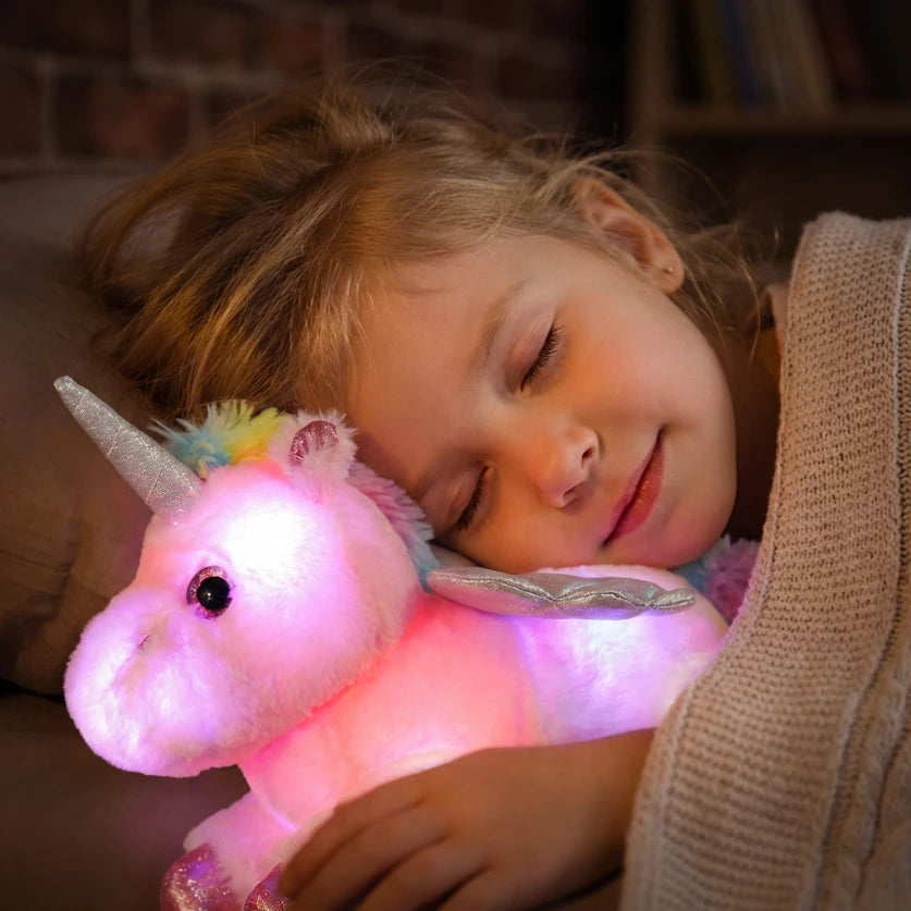 Gros plan d'un enfant dormant paisiblement la joue contre sa veilleuse licorne rose, diffusant une lumière douce pour chasser la peur du noir.